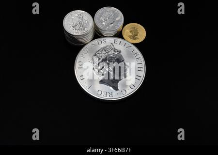 Silberbarrenmünze mit Stapeln von Silbermünzen und einer Goldmünze auf schwarzem Hintergrund. Konzept von Edelmetallen, Investition, Reichtum, Sparen Stockfoto