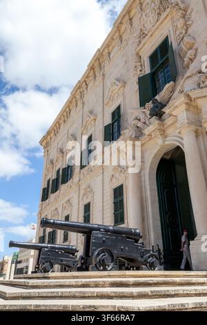 Historische Kanonen flankieren den barocken Eingang der Auberge de Castille in Valletta, Malta, ein Wachposten steht Wache an der Tür des Premierministeramtes Stockfoto