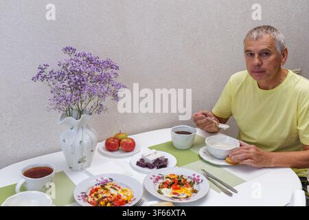 Hochwinkelaufnahme eines reifen Mannes, der an einem Küchentisch sitzt und hausgemachten Haferbrei und gebratene Eier als gesundes Frühstück isst. Stockfoto
