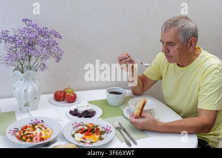 Hochwinkelaufnahme eines reifen Mannes, der an einem Küchentisch sitzt und hausgemachten Haferbrei und gebratene Eier als gesundes Frühstück isst. Stockfoto