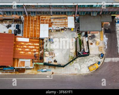 Luftbild des Logistikgebiets Serravalle mit Industriegebäuden mit verrosteten Dächern, Lagerhöfen mit Holzpaletten und einer Asphaltstraße i Stockfoto