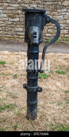 Alte Wasserpumpe steht in einer offenen Fläche nahe einer Steinmauer und grasbewachsenem Boden Stockfoto