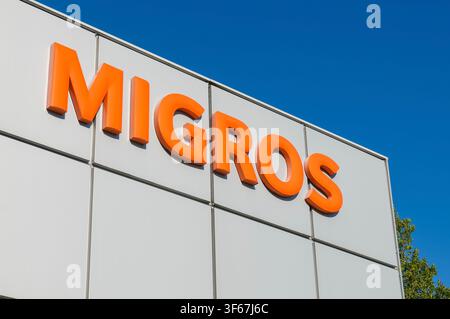 San Antonino, Ticino, Schweiz – 3. Juli 2026: Migros-Orange-3D-Firmenlogo-Schild, Nahaufnahme aus niedrigem Winkel, montiert an der weißen Außenfassade von Stockfoto