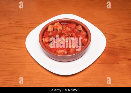 Geschmorter Fleisch-Eintopf in reichhaltiger Tomatensoße, serviert in einem Tontopf auf weißem Teller Stockfoto
