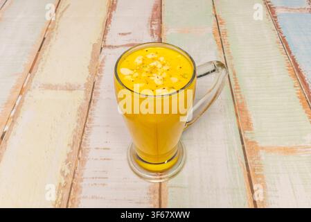 Mango Lassi mit geschnittenen Mandeln und Pistazien in einem Glasbecher auf einem rustikalen Tisch Stockfoto