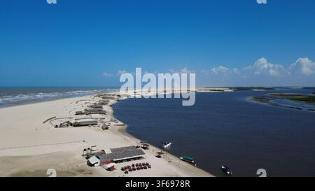 Luftbilddrohnenaufnahme eines Flusses, der in den Atlantischen Ozean mündet, in Lençóis Maranhenses, Maranhão, Brasilien. Weiße Sanddünen, Fischerdorf und Mangroven Stockfoto