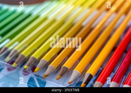 Eine helle und lebendige Nahaufnahme, die sich auf warmtonige Farbstifte konzentriert, darunter lebendige Gelbtöne, Orangetöne und Rottöne, die ordentlich in einer klaren Anordnung angeordnet sind Stockfoto