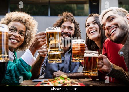 Verschiedene Freunde haben gemeinsam ein Abendessen - Multikulturelle junge Leute haben Spaß, während sie Biergläser in einer Brauerei-Pub-Bar anstoßen - Happy Hour, Feier Stockfoto