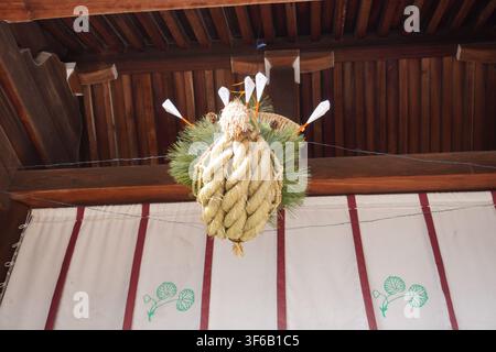 Ein bezauberndes saisonales Tafelaufsatz, das von einem Holzbalken hängt. Dieses rustikale Arrangement zeigt immergrüne Zweige, gewebte Stroh-Akzente und dekorative Wei Stockfoto