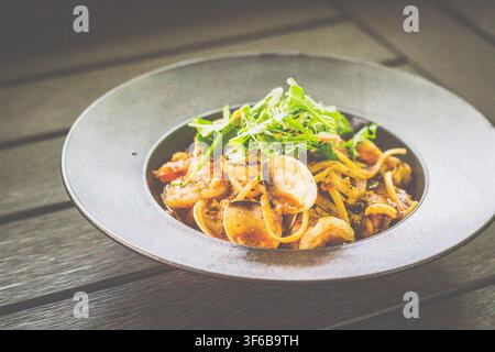 Sambal-Meeresfrüchte-Pasta mit Garnelen, Tintenfischen, Muscheln, Venusmuscheln und Sambal-Marinara-Sauce, serviert auf einem schwarzen Teller Stockfoto