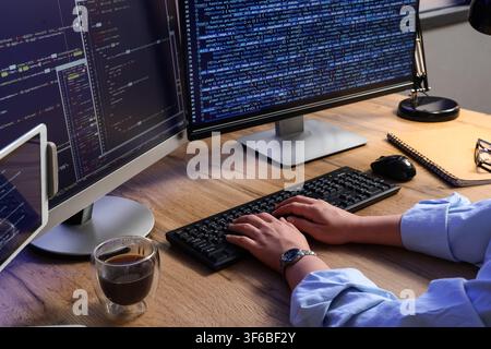 Programmierhände, die auf einer Tastatur tippen, mit mehreren Computerbildschirmen, die Code-Softwareentwicklung und IT anzeigen, dieses Setup Softwareentwicklungsinfo Stockfoto