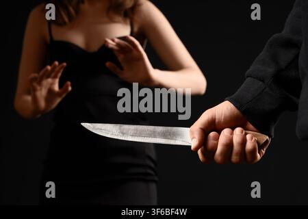 Mann hält ein Messer und bedroht eine Frau in einem schwarzen Kleid, Konzept für häusliche Gewalt und Kriminalität, dunkler Hintergrund Stockfoto