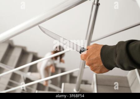 Mans Hand, die ein Messer hält, droht einer Frau, die die Treppe hinunterläuft, häusliche Gewalt und Verbrechen Stockfoto