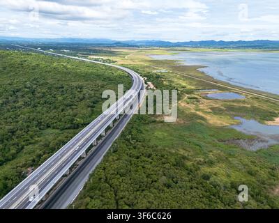Dronen-Luftbild einer hochgelegten Autobahn, die einen üppigen Wald und eine Berglandschaft unter dramatischen Wolken überquert, Die moderne Transportinfrastruktur a Stockfoto
