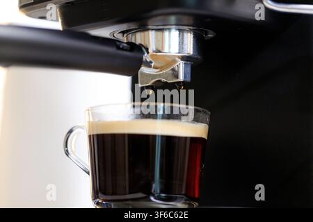 Nahaufnahme einer Espressomaschine, die frisch extrahierten schwarzen Kaffee in eine klare Glastasse brüht, wobei die Kaffeezubereitung hervorgehoben wird Stockfoto
