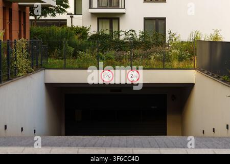 Eingang zu einer unterirdischen Parkgarage eines modernen Wohngebäudes mit Höchsthöhenzeichen und Grünpflanzen über der Einfahrrampe Stockfoto