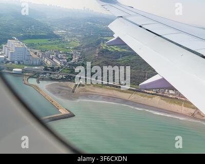Luftbild aus einem Flugzeugfenster, das den Flügel, die Küste, das blaue Meer, den Strand und die Stadtlandschaft von Tokio, Japan, zeigt. Stockfoto
