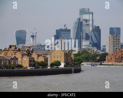Eine Weitwinkel-Landschaftsperspektive zeigt eine Passagierfähre, die am 24. Juli 2026 eine Biegung der Themse navigiert. Die hoch aufragenden modernen Wolkenkratzer des Finanzdistrikts der City of London erheben sich gegen den Horizont in der Ferne, eingerahmt von den niedrigen Wohnhäusern von Rotherhithe am linken Ufer und den zeitgenössischen Wasserwohnungen von Limehouse am rechten Ufer Stockfoto