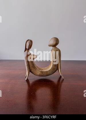 Stilisierte Skulptur zweier abstrakter menschlicher Figuren, die sich gegenüber sitzen auf einer Holzoberfläche vor einem schlichten Hintergrund. Stockfoto