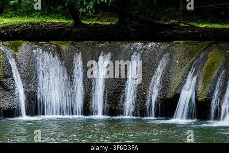 Süsswasser, das über dunkle, moosbedeckte Felsen fließt, bildet kleine Kaskaden und schafft eine ruhige Szene in einer grünen natürlichen Umgebung, Namtok Kapo Forest Stockfoto