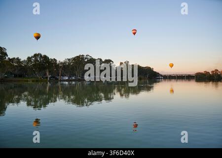 Drei Heißluftballone fliegen über den Murray River an einem ruhigen Winterabend. Fotografiert von der viktorianischen Seite aus, mit Blick auf Buronga NSW, und th Stockfoto