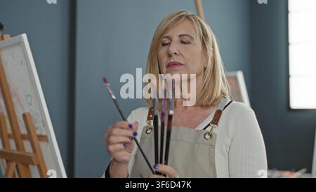 Frau Malerin hält Pinsel in der Hand, während sie Spitzen an einer Staffelei in einem Atelier betrachtet; ruhige Konzentration. Stockfoto
