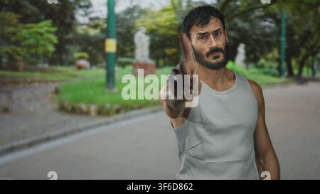 Mann zeigt mit dem Finger auf dem Straßenweg in einem Park, ärmelloses Hemd und angespannte Haltung; Wutkonfrontation. Stockfoto