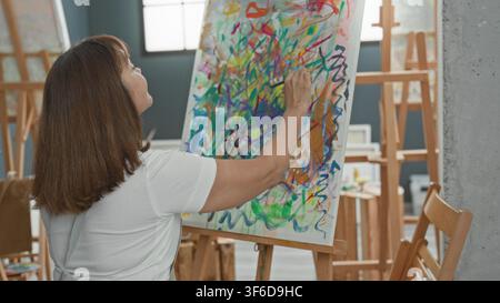 Malerin steht an der Staffelei, rechte Hand malt dicke bunte Striche auf Leinwand, während sie Palette hält, Rückansicht im Kunststudio; Konzentration cr Stockfoto