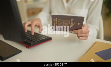 Frau hält Reisepass und tippt an einer Tastatur am Flughafen-Schalter mit sichtbarlichem Monitor und Ordner; professioneller Fokus. Stockfoto