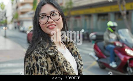 Frau mit Brille, lächelnd und über die Schulter schauend, Leopardenmantel auf der Straße sichtbar; Selbstvertrauen urbaner. Stockfoto