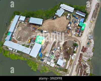 Luftaufnahme einer Baustelle mit schweren Maschinen, Betonmischern und Sandhaufen auf einer von Wasser umgebenen Halbinsel in Kishoreganj, Dh Stockfoto