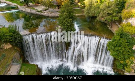 Luftaufnahme des Pliva-Wasserfalls, der in den Fluss stürzt, mit üppigen grünen Bäumen und steinigen Ufern in Jajce, Föderation Bosnien, Bosnien und Herzegowina. Stockfoto