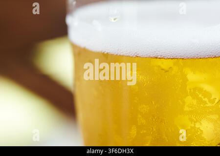 Makro-Nahaufnahme von kaltem frischem Leichtbier in einem transparenten Glas mit weißem Schaumkopf und Kondenswassertropfen auf der Außenseite. Stockfoto