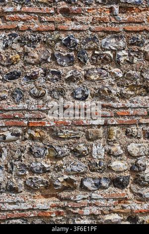 Vollständiger vertikaler Abschnitt einer antiken römischen Mauer mit abwechselnden Bändern aus roten Keramikfliesen und geknapptem Feuerstein in Burgh Castle in Norfolk, England. Stockfoto