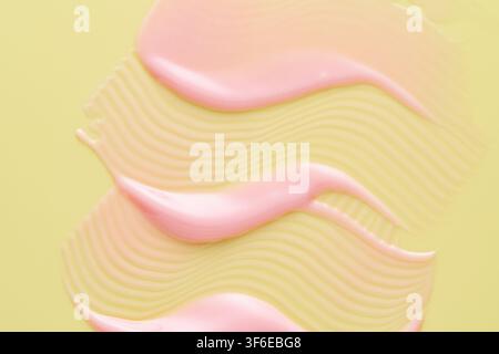 Nahaufnahme einer abstrakten Komposition aus glänzenden rosa Lipgloss-Flecken, die über einer welligen Cremetextur auf einem weichen gelben Hintergrund geschichtet sind, was Schönheitskosmetik hervorruft, s Stockfoto