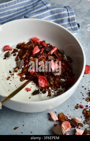 Gesunde Joghurt-Schüssel mit Schokoladen-Granola, gefrorenen Erdbeeren, frischen Beeren und geschnittener Banane Stockfoto
