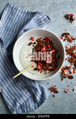 Gesunde Joghurt-Schüssel mit Schokoladen-Granola, gefrorenen Erdbeeren, frischen Beeren und geschnittener Banane Stockfoto