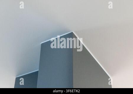 Ein minimalistisches Innendesign mit einer scharfen Ecke, an der eine graue Wand auf eine weiße Decke trifft, beleuchtet von sanftem indirektem Licht Stockfoto