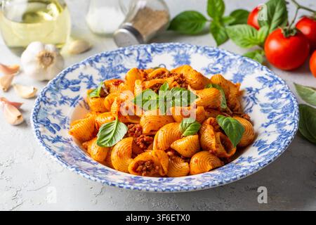 Köstliche Pipe Rigate Pasta mit Bolognese-Fleischsauce und frischen Basilikumblättern Stockfoto
