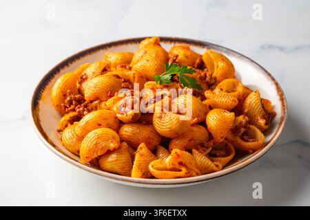 Köstliche Pipe Rigate Pasta mit Bolognese-Fleischsauce und frischen Basilikumblättern Stockfoto