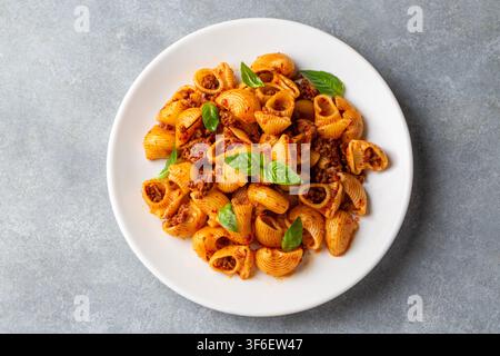 Köstliche Pipe Rigate Pasta mit Bolognese-Fleischsauce und frischen Basilikumblättern Stockfoto