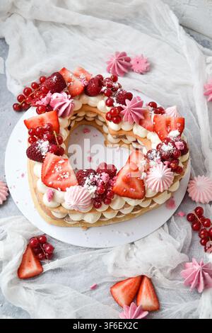 Herzförmiger Schichtkuchen, dekoriert mit Erdbeeren, roten Johannisbeeren und rosa Baiser Stockfoto