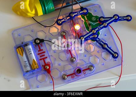 Eine Nahaufnahme einer transparenten elektronischen Leiterplatte mit Batterien, Drähten und einer leuchtenden Glühbirne, die grundlegende elektrische Prinzipien demonstriert Stockfoto
