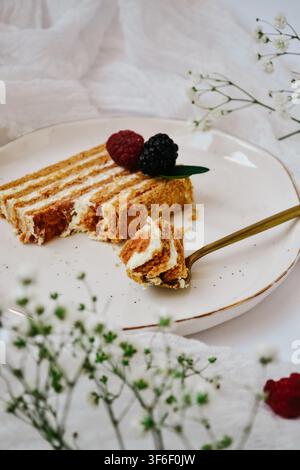 Scheibe geschichteter Honigkuchen Medovik mit Himbeere und Brombeere auf keramikplatte mit goldlöffel Stockfoto