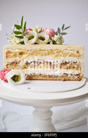 Querschnitt eines geschichteten Biskuitkuchens mit weißer Frischkäse-Zuckerglasur, verziert mit frischen Eustoma-Blüten auf einem Kuchenständer Stockfoto