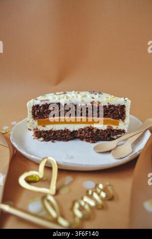Scheibe Schokoladenspongekuchen mit Mangogelée-Schicht und weißer Sahne auf beigem Hintergrund, romantisches Urlaubskonzept Stockfoto