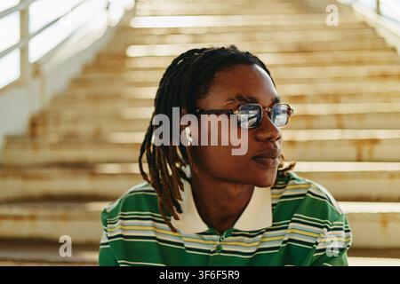 Schwarzer Mann mit Brille und Ohrstöpseln sitzt draußen auf einer Treppe Stockfoto