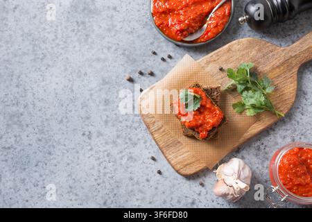 Scheibe Roggenbrot und hausgemachte Pasta ajvar. Gemüsesauce oder Kaviar gebackener roter Paprika auf Grau. Balkan-Appetithäppchen. Horizontale Orientierung Stockfoto