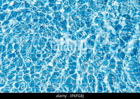 Das Sonnenlicht bricht sich im klaren blauen Wasser und erzeugt schimmernde Muster auf der gefliesten Oberfläche eines Schwimmbeckens Stockfoto