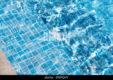 Das Sonnenlicht bricht sich durch klares Wasser und erzeugt dynamische Muster auf einem gefliesten Poolboden Stockfoto